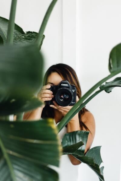 Woman holding camera behind plant